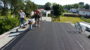 Two people applying tar paper to roof